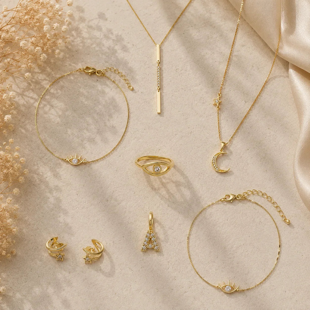 Flat lay of Ma Vie Jewelry collection with 18k gold-filled necklaces, rings, earrings, and bracelet on cream silk fabric