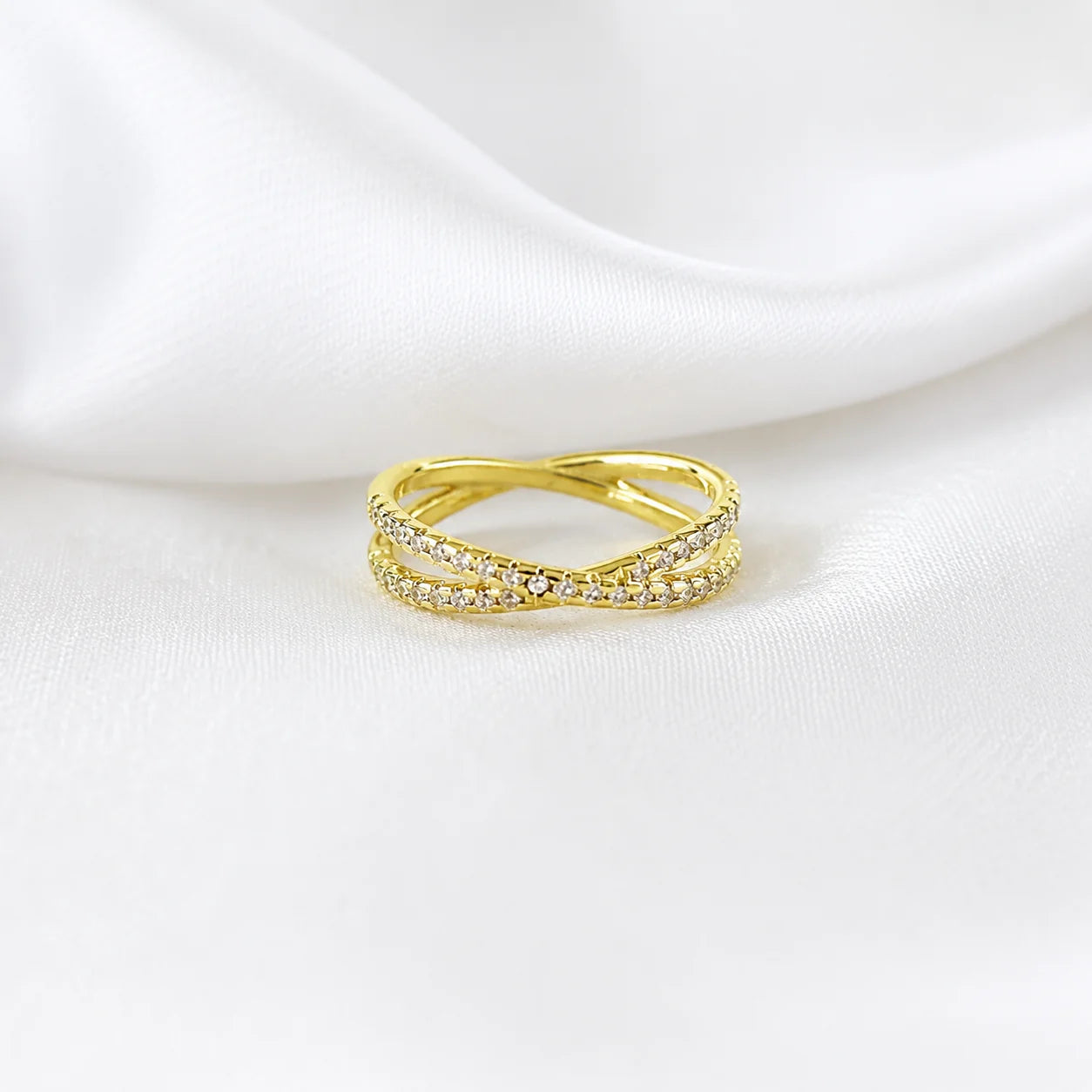 CZ X ring in 18k gold filled lying on white silk, crossover pavé band