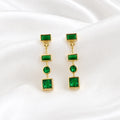 Flat lay of Ma Vie emerald drop earrings on cream silk, 18k gold filled green CZ geometric