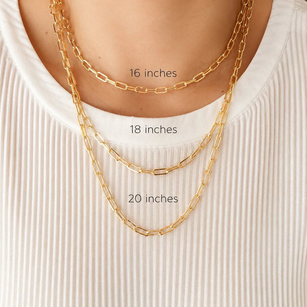 Three gold filled paperclip chain necklaces layered at staggered lengths on cream ribbed fabric