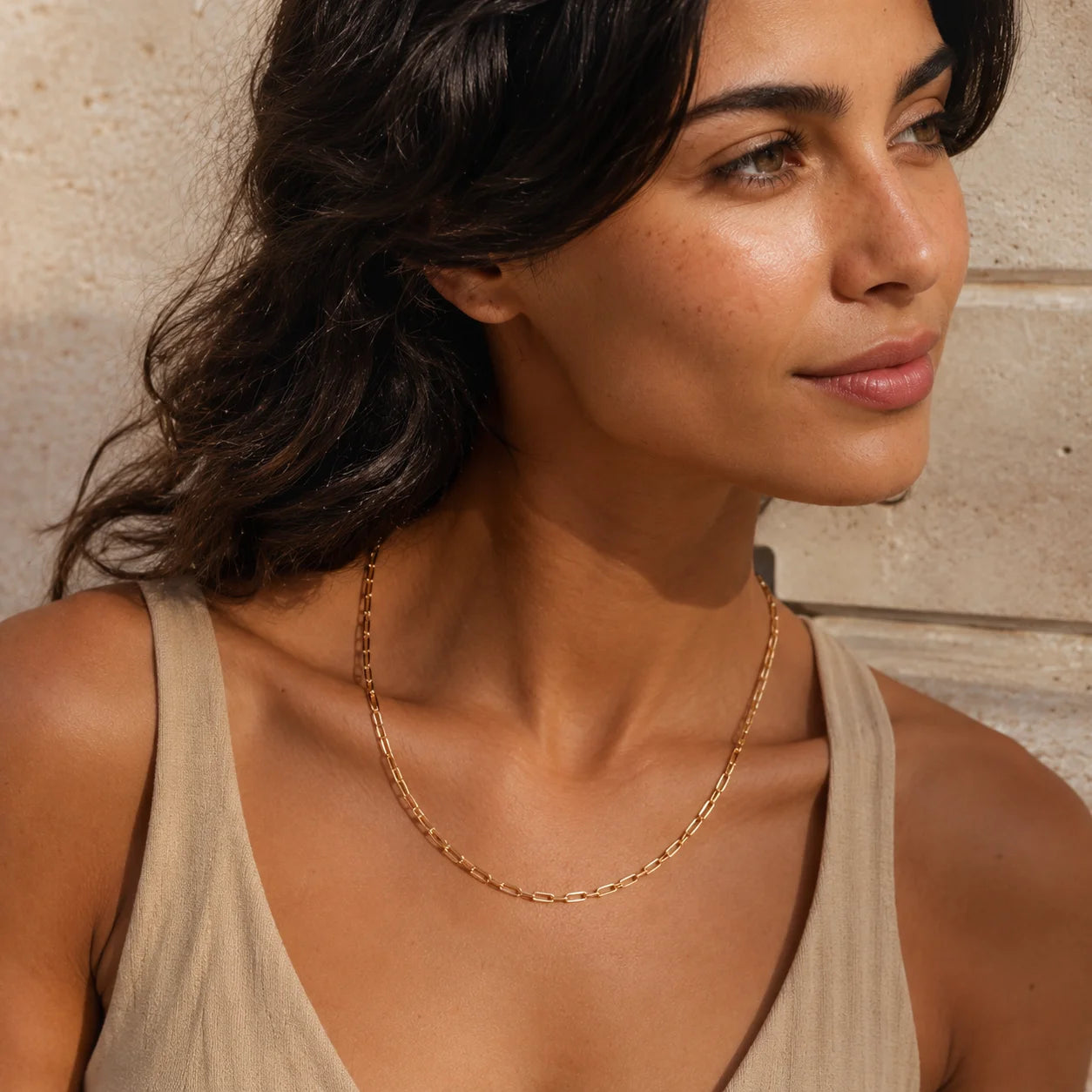 Dark haired woman wearing gold paperclip chain necklace, side profile at collarbone