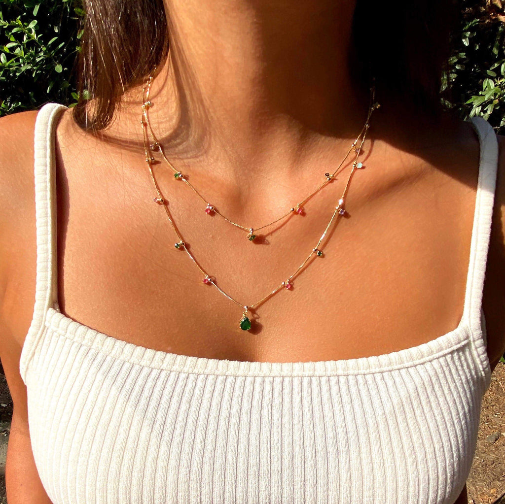 Multicolor layered teardrop necklace worn with a white top outdoors