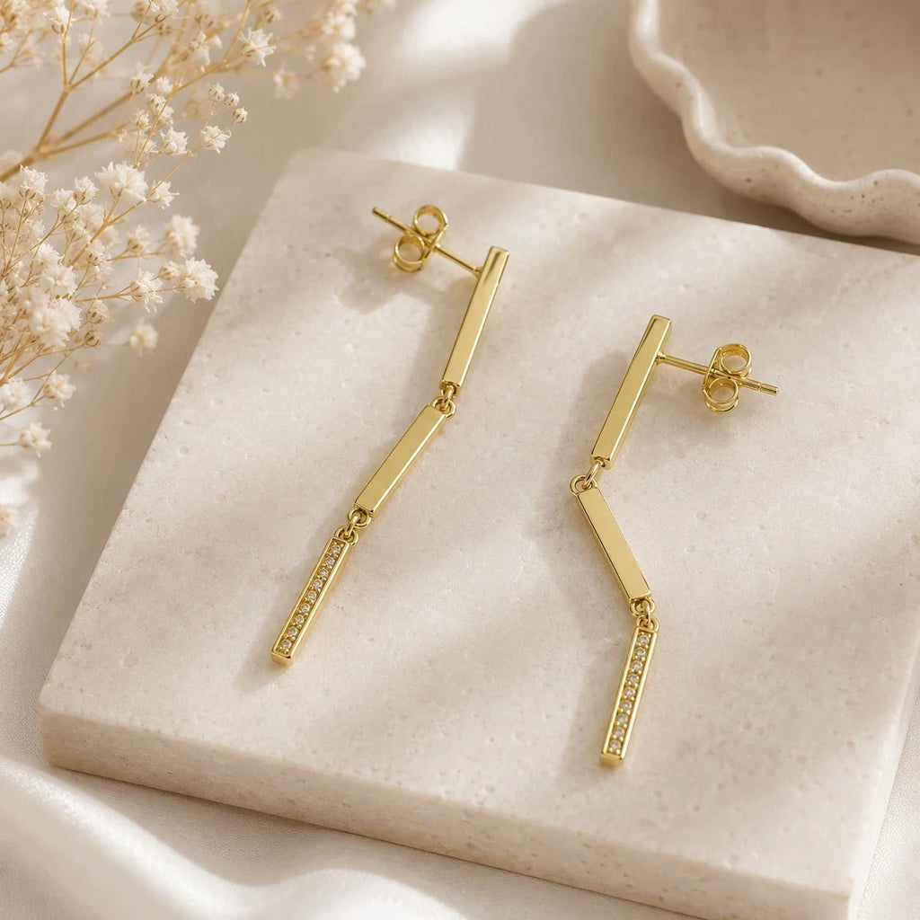 Close-up of 18K gold-filled linear bar drop earrings on cream fabric
