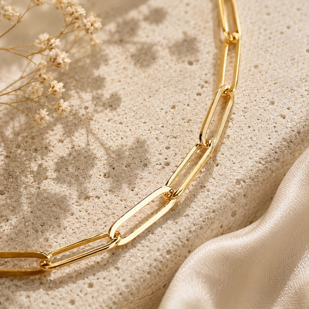 Flat lay of Ma Vie paperclip chain anklet on cream silk fabric, 18k gold filled dainty