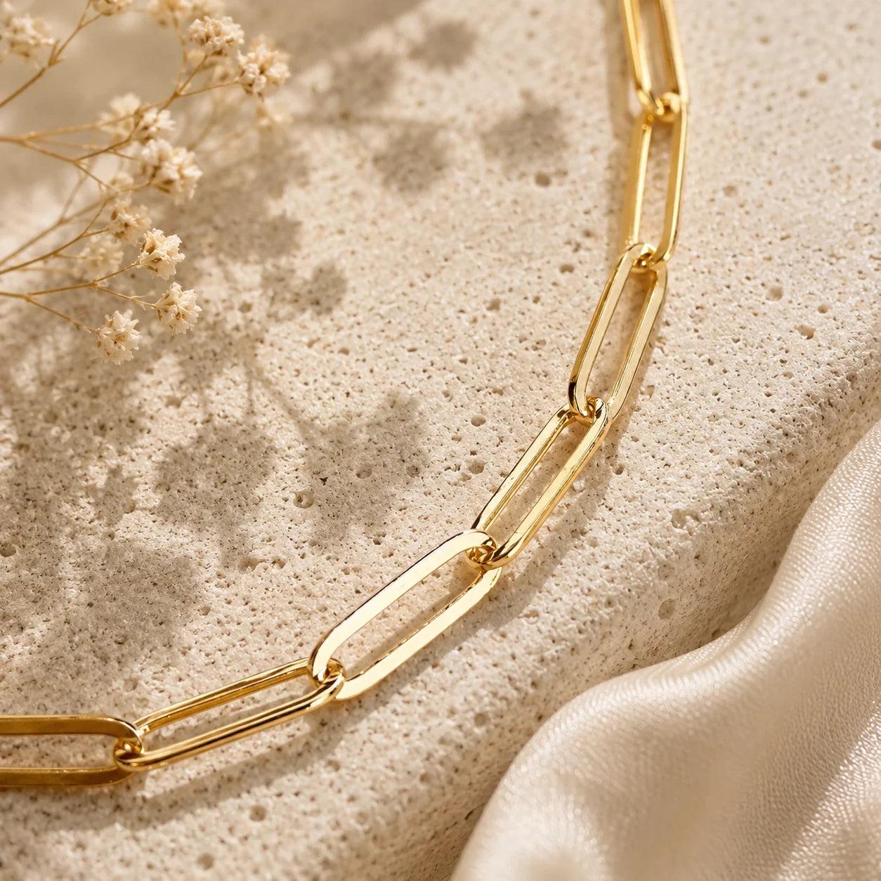 Flat lay of Ma Vie paperclip chain anklet on cream silk fabric, 18k gold filled dainty