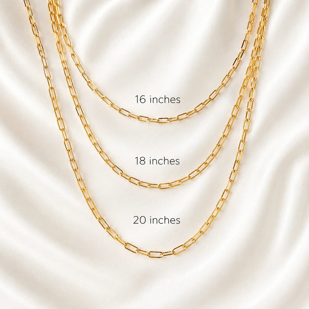Layered 18k gold filled paperclip link necklaces displayed flat on ivory silk, three lengths