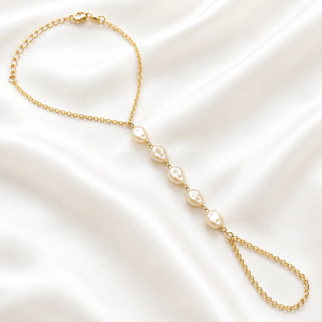 Flat lay of Ma Vie pearl hand chain bracelet on cream silk, 18k gold filled with baroque pearl