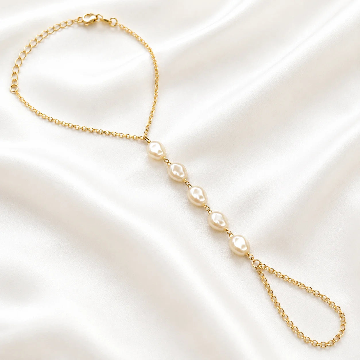 Flat lay of Ma Vie pearl hand chain bracelet on cream silk, 18k gold filled with baroque pearl